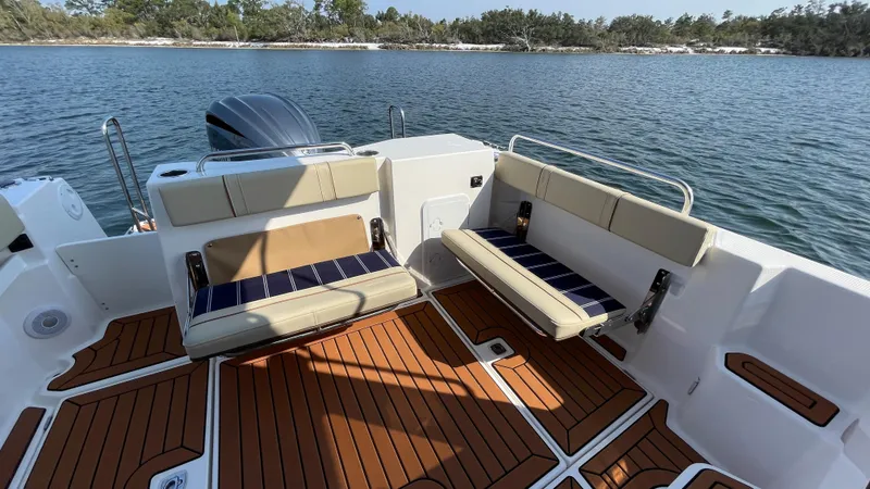 Slide: The Image of 2025 Ranger Tugs R-25 boat interior with cushioned seating and wooden deck, overlooking serene water. - 14