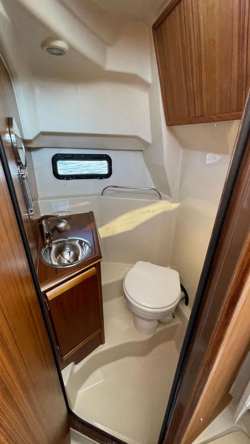 Slide: The Image of Compact bathroom in 2025 Ranger Tugs R-25 with sink, toilet, and wood cabinetry. - 33