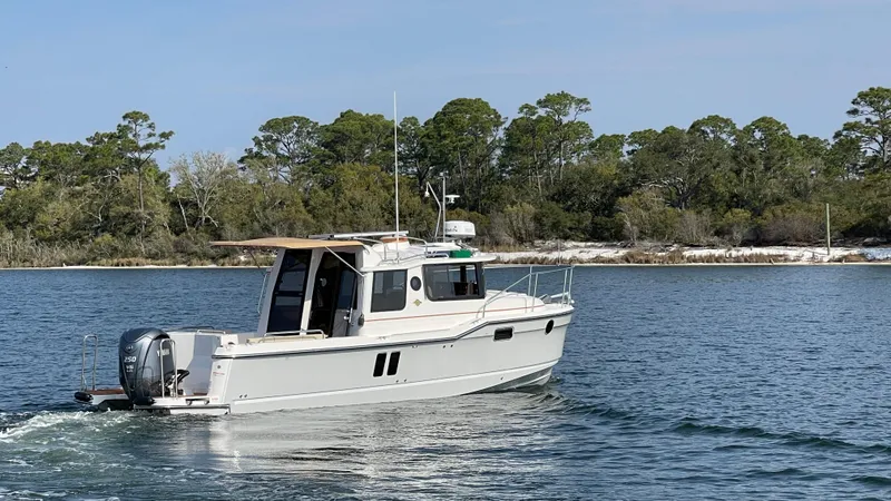 Slide: The Image of 2025 Ranger Tugs R-25 cruising on a serene lake with lush green shoreline. - 5