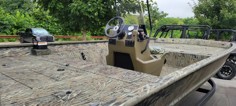 Slide: The Image of 2025 Tracker Grizzly 2072 CC boat with camouflage design, parked outdoors near trees. - 2