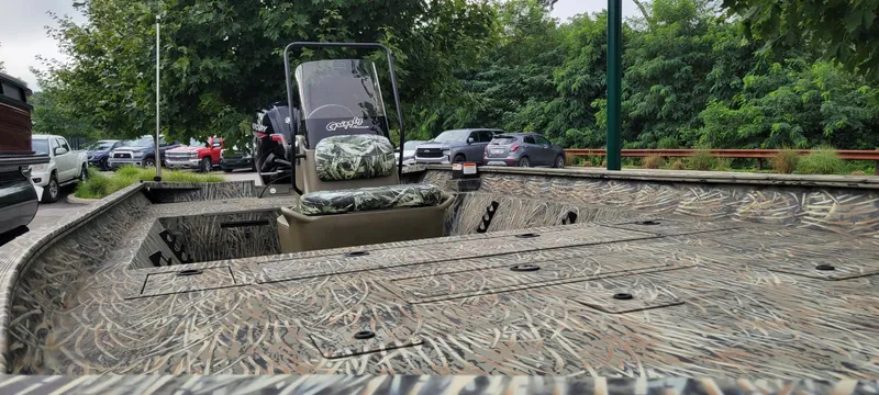 Slide: The Image of 2025 Tracker Grizzly 2072 CC boat with camouflage design, parked outdoors near trees and cars. - 3