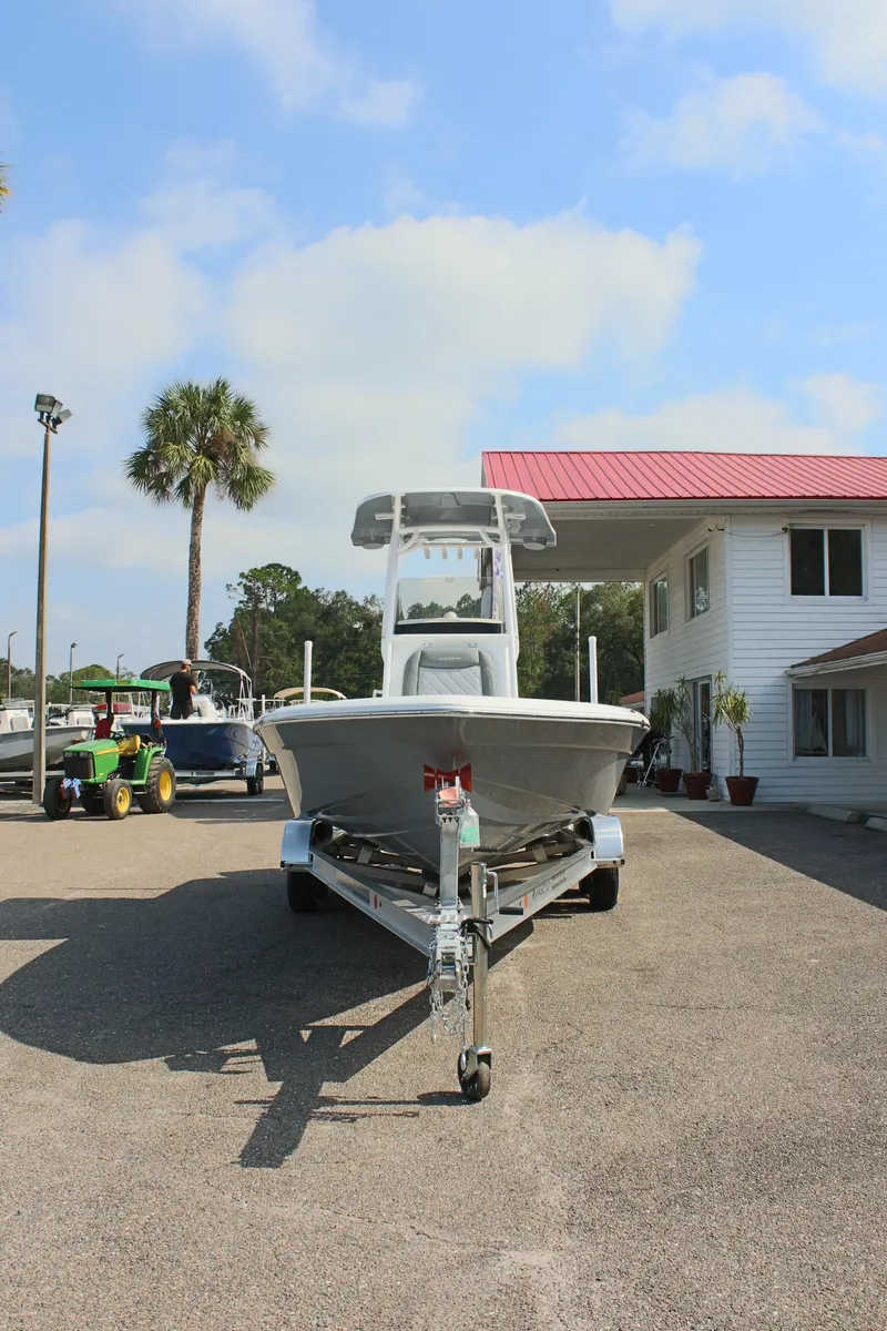 Slide: The Image of 2025 NauticStar 224 Bay boat on trailer, parked outdoors near a white building. - 3