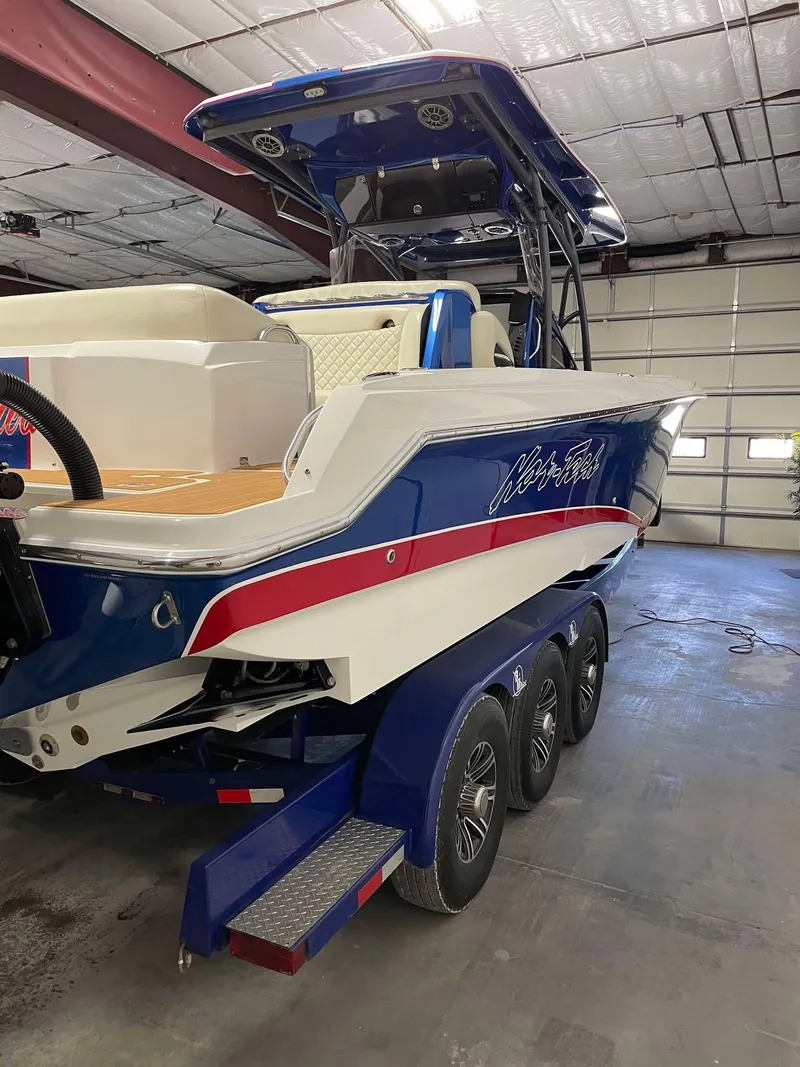 Slide: The Image of 2015 Nor-Tech 340 Sport Center Console boat in a garage, featuring a blue and white design. - 7