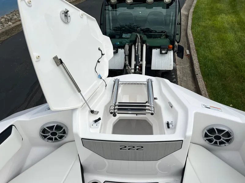Slide: The Image of 2025 Yamaha Boats 222SE with open storage compartment and ladder, parked near a green vehicle. - 17