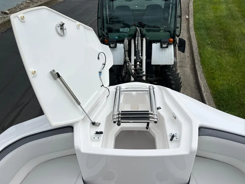 Slide: The Image of 2025 Yamaha Boats AR250 with open storage compartment, parked near a tractor on a paved road. - 19