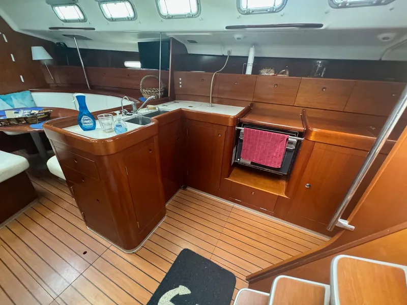 Slide: The Image of Interior of 2004 Beneteau First 47.7 yacht, featuring a wooden kitchen and seating area. - 19