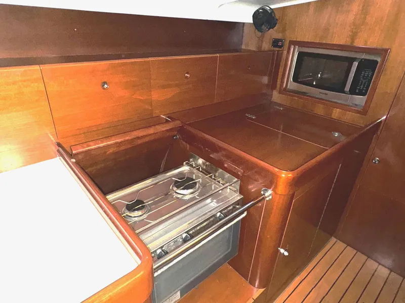 Slide: The Image of Beneteau First 47.7 2004 yacht kitchen with stove, microwave, and wooden cabinetry. - 20