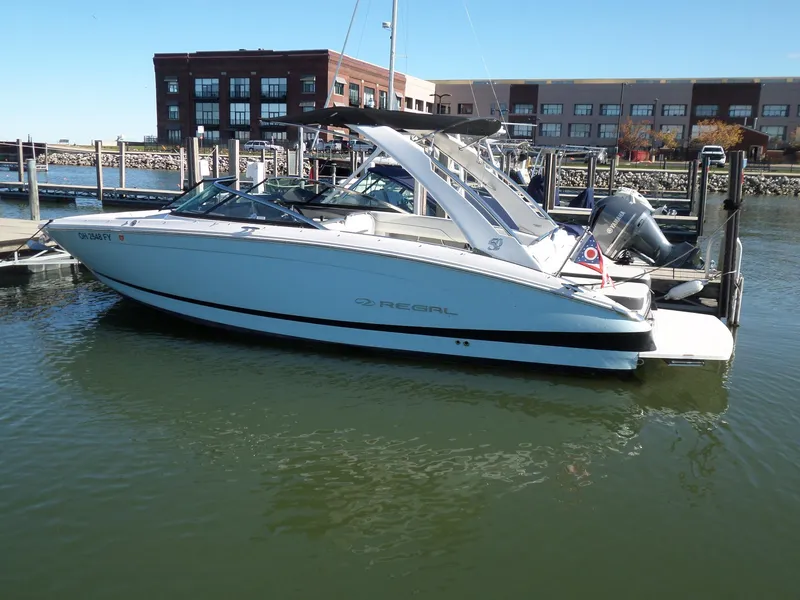 Slide: The Image of 2020 Regal LS6 boat docked in marina, clear day, modern buildings in background. - 2