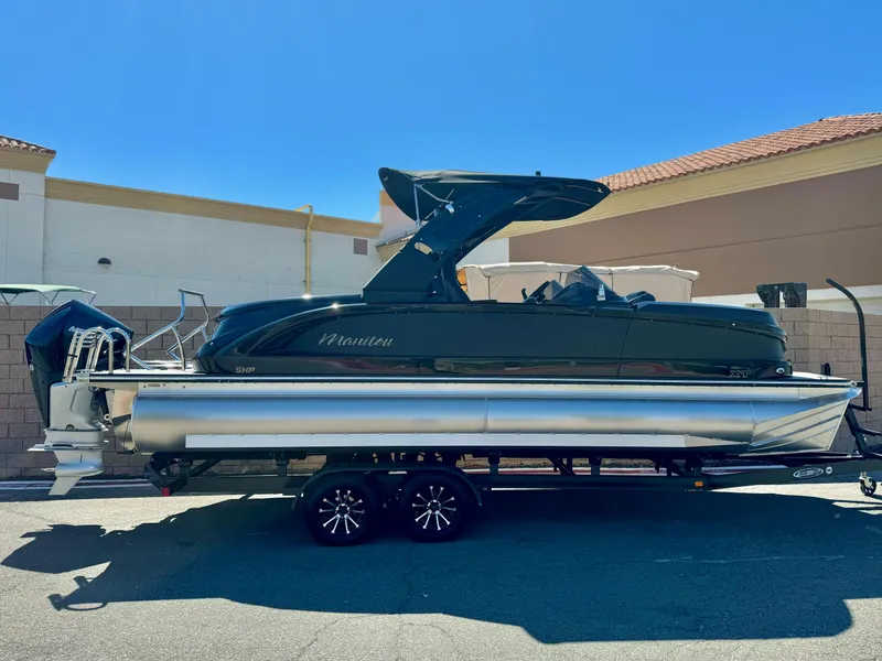 The Image of 2024 Manitou 23 XT RFXW pontoon boat on trailer, parked outdoors. - 0