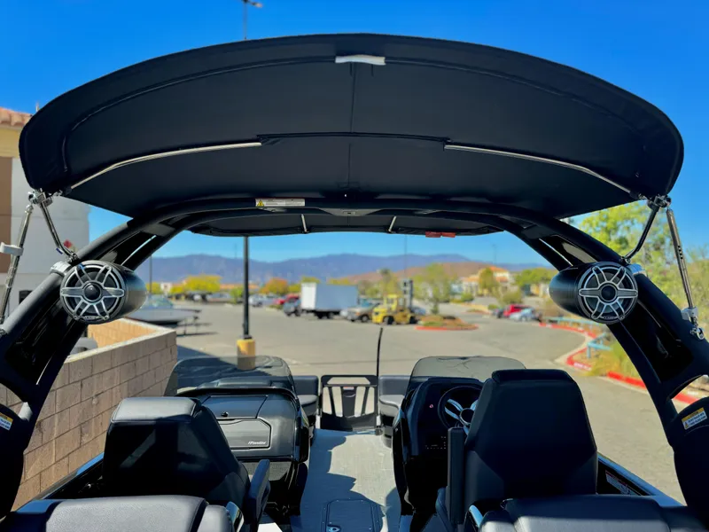 Slide: The Image of 2024 Manitou 23 XT RFXW boat interior with speakers and canopy, parked outdoors. - 19