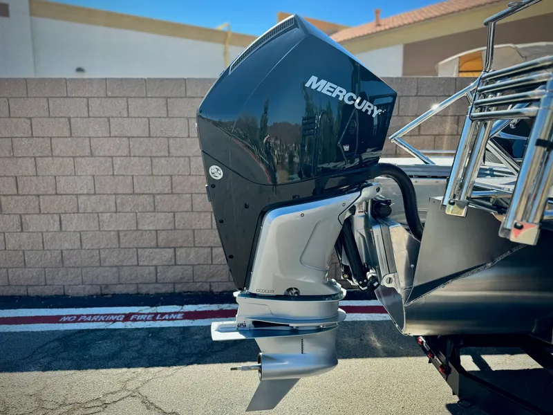 Slide: The Image of 2024 Manitou 23 XT RFXW with Mercury outboard motor, parked near a brick wall. - 7