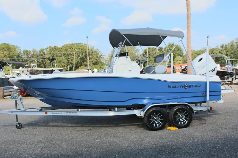 The Image of 2025 NauticStar 211 Hybrid boat on trailer, blue hull, parked outdoors. - 1