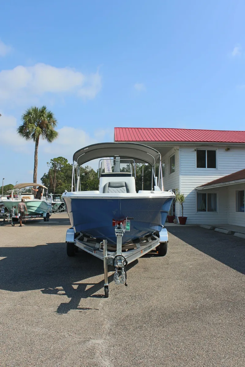 Slide: The Image of 2025 NauticStar 211 Hybrid boat on trailer, parked near a building with a red roof. - 3