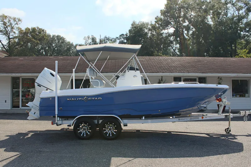 Slide: The Image of 2025 NauticStar 211 Hybrid boat on trailer, blue hull, parked outdoors. - 5