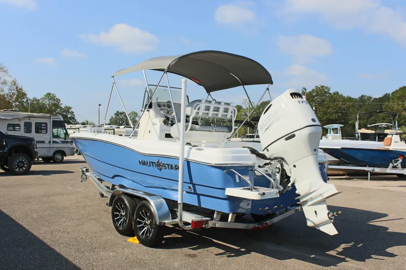 Slide: The Image of 2025 NauticStar 211 Hybrid boat on trailer, blue and white design, parked outdoors. - 9