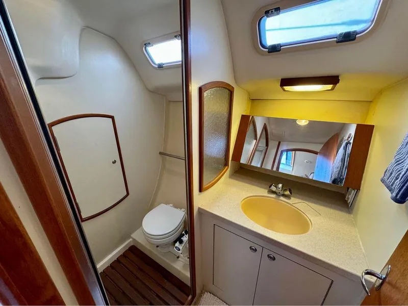 Slide: The Image of 2002 Hunter 356 yacht bathroom with toilet, sink, mirror, and porthole windows. - 14