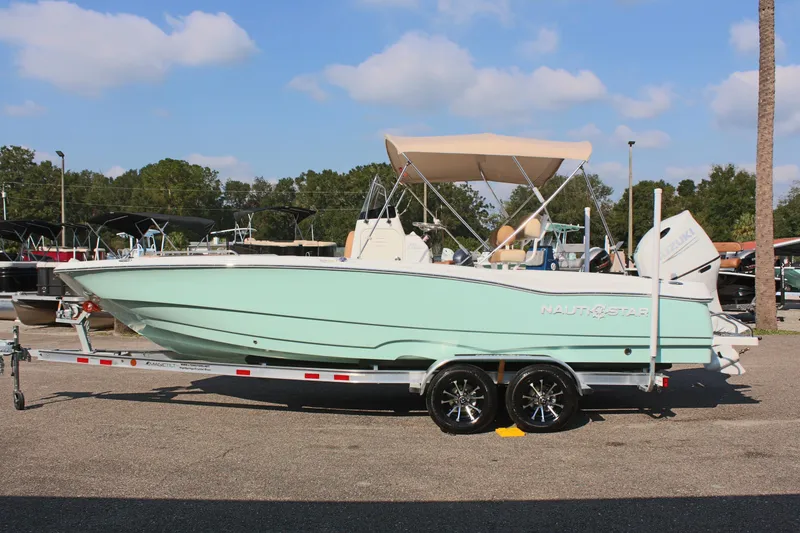 The Image of 2025 NauticStar 231 Hybrid boat on trailer, light blue hull, parked outdoors. - 1