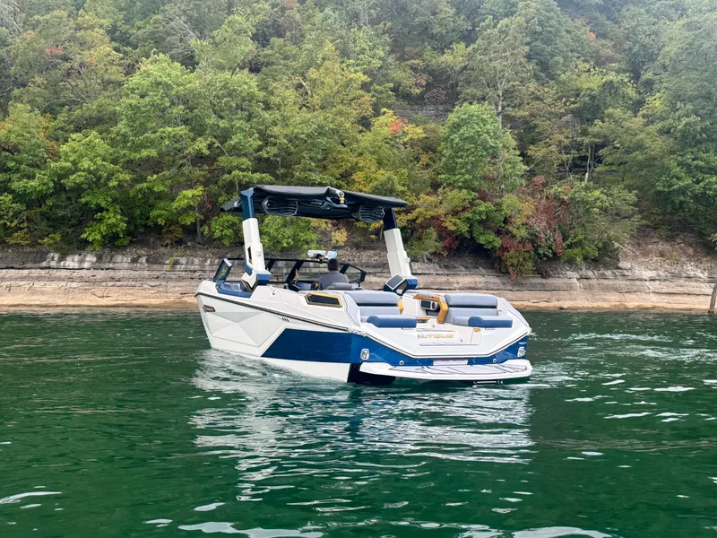 Slide: The Image of 2024 Nautique Super Air Nautique G25 Paragon on a serene lake with lush forest backdrop. - 4