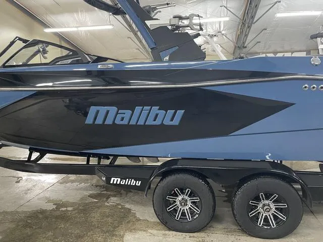 Slide: The Image of 2024 Malibu 23 LSV boat in a showroom, featuring sleek design and dual-axle trailer. - 6