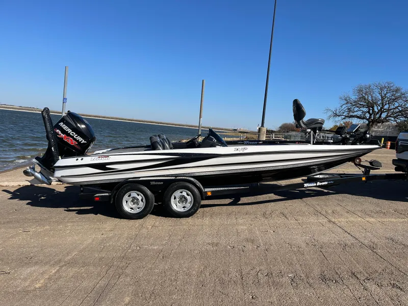 Slide: The Image of 2013 Triton 21 HP boat on trailer by the water, clear blue sky. - 23