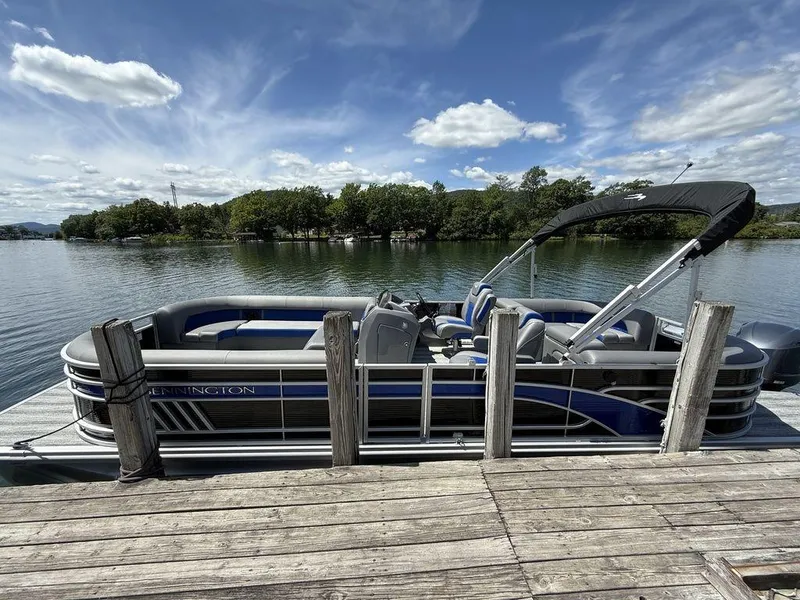 The Image of 2025 Bennington 25LSR pontoon boat docked on a serene lake under a partly cloudy sky. - 0