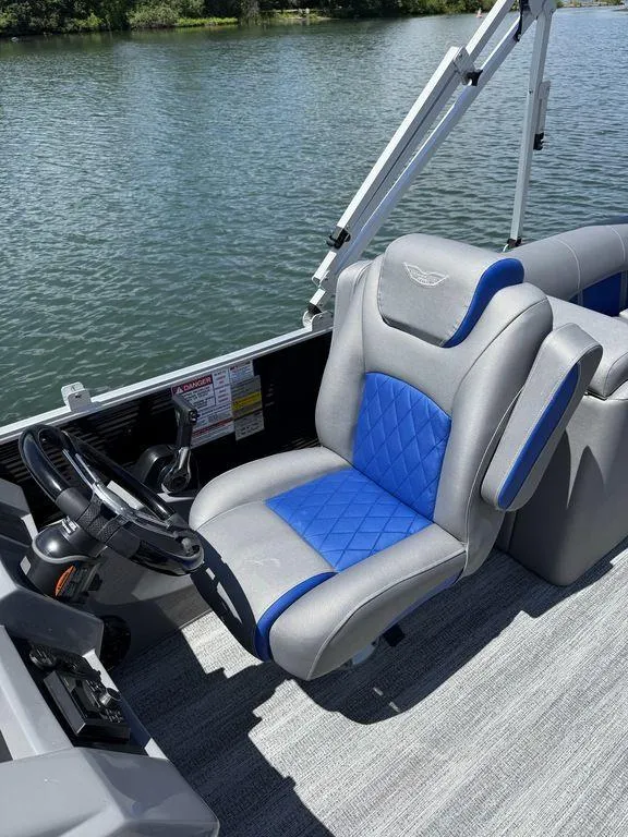 Slide: The Image of 2025 Bennington 25LSR boat interior with blue and gray captain's chair on a lake. - 14