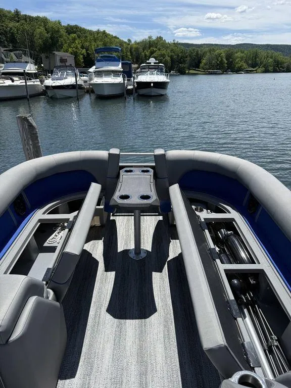 Slide: The Image of 2025 Bennington 25LSR pontoon boat interior with seating and table, docked by a serene lake. - 18