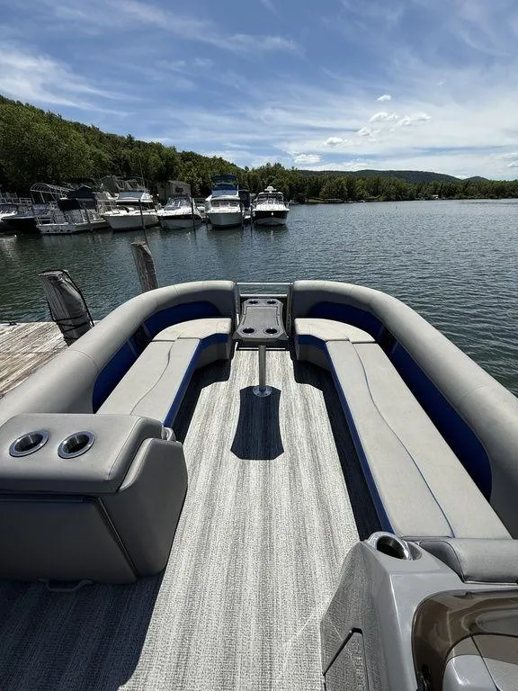 Slide: The Image of 2025 Bennington 25LSR pontoon boat interior with seating, docked on a scenic lake. - 23