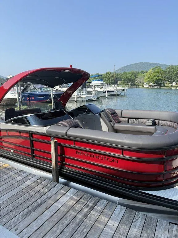 Slide: The Image of 2025 Bennington 25RSBWAX1 pontoon boat docked on a sunny lake with scenic background. - 1
