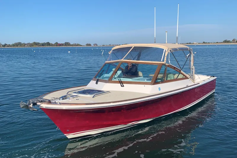 Slide: The Image of 2013 Hunt Yachts Harrier 25 boat on calm water, featuring a red hull and tan canopy. - 2