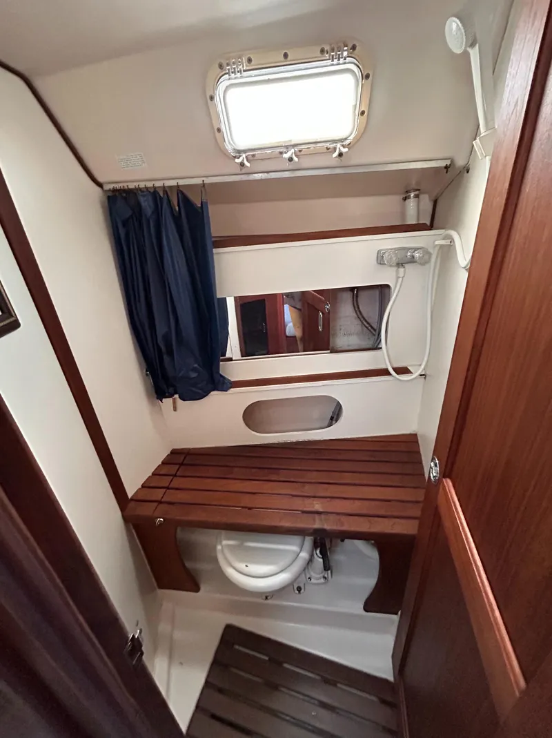 Slide: The Image of 1983 Hunter 34 sailboat bathroom with wooden bench, shower, and porthole window. - 48