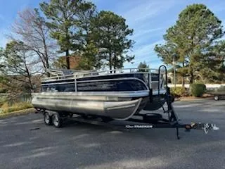 Slide: The Image of 2025 Sun Tracker Fishin' Barge 22 XP3 pontoon boat on trailer, parked outdoors. - 2