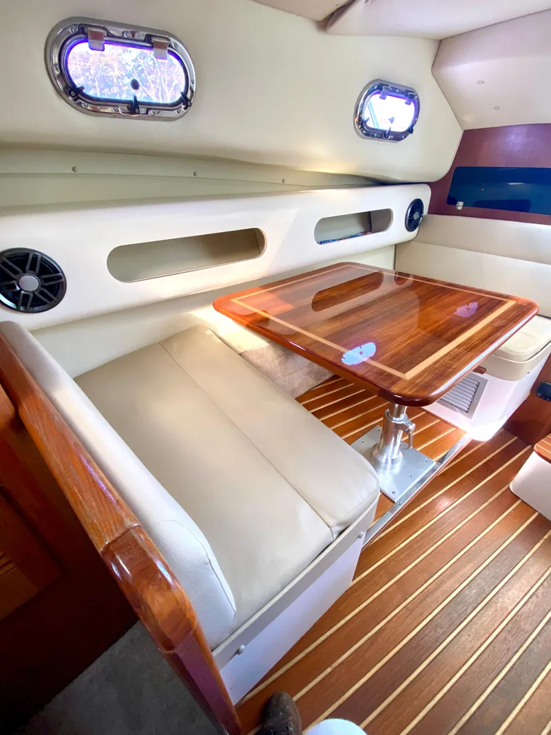 Slide: The Image of 2004 Pursuit 3100 Offshore cabin with wooden table, beige seating, and porthole windows. - 18
