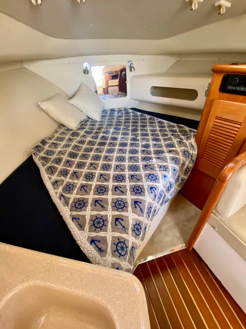Slide: The Image of 2004 Pursuit 3100 Offshore cabin with nautical-themed bedding and wooden interior accents. - 21