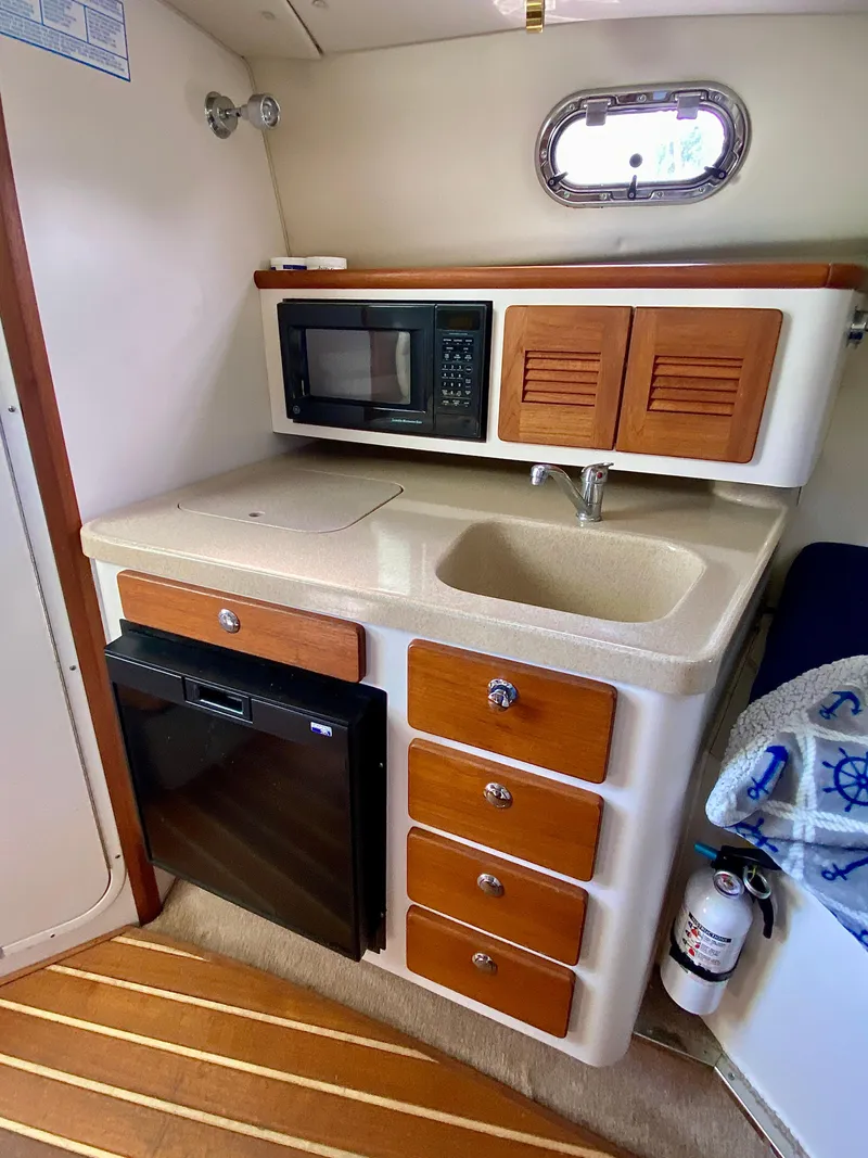 Slide: The Image of 2004 Pursuit 3100 Offshore boat kitchenette with microwave, sink, and storage drawers. - 22