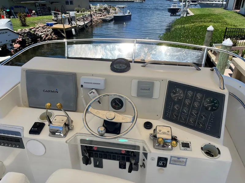 Slide: The Image of 1994 Tiara Yachts 3600 Convertible Sportfish helm with Garmin navigation, docked by a scenic waterfront. - 20