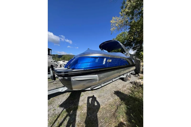 The Image of 2025 Bennington 25QXSBWA pontoon boat with blue exterior, parked on a trailer under clear skies. - 0