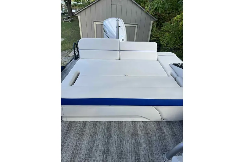Slide: The Image of 2025 Bennington 25QXSBWA boat with white and blue seating, near a shed. - 10