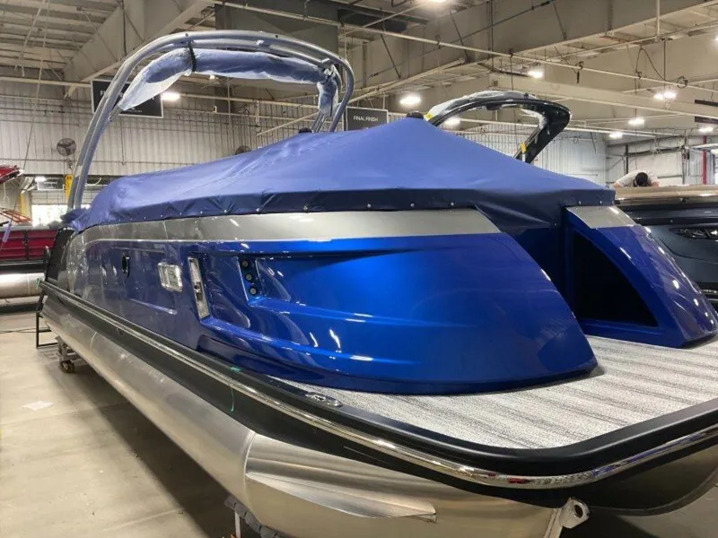 Slide: The Image of 2025 Bennington 25QXSBWA pontoon boat with blue cover in a showroom. - 2