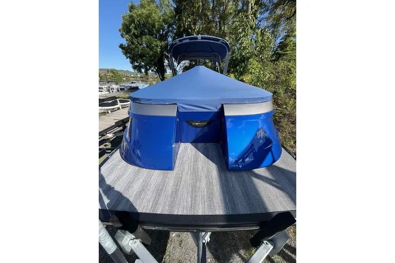 Slide: The Image of 2025 Bennington 25QXSBWA boat with blue cover, docked near trees. - 5