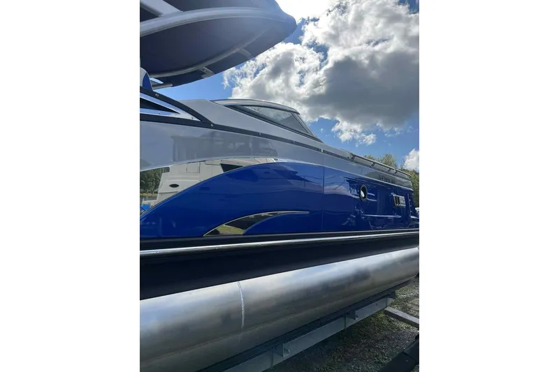 Slide: The Image of 2025 Bennington 25QXSBWA pontoon boat with sleek blue and silver design under cloudy sky. - 6