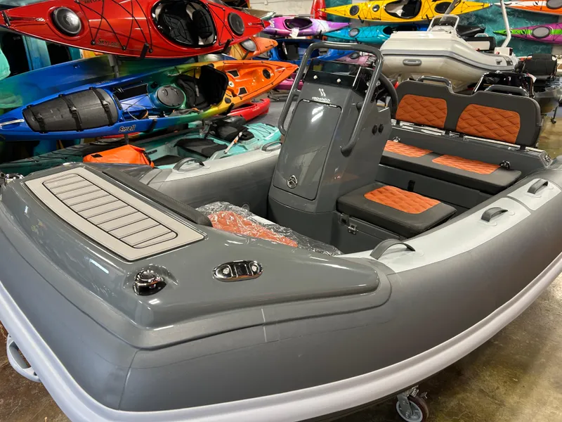 Slide: The Image of 2024 Highfield Sport 330 inflatable boat with orange seats, displayed indoors among colorful kayaks. - 8