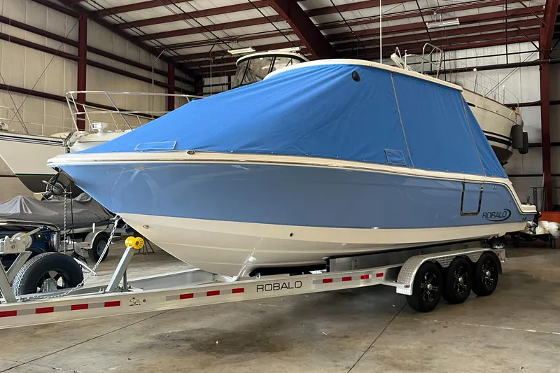 Slide: The Image of 2023 Robalo R 272 boat on trailer, covered in blue tarp, stored indoors. - 13