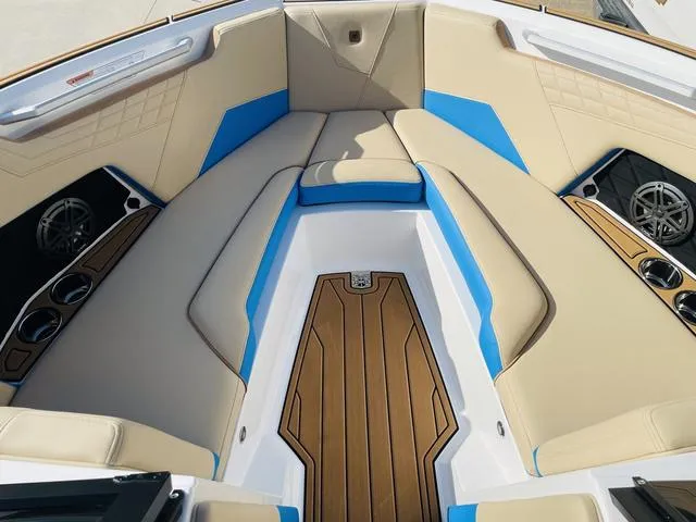 Slide: The Image of 2024 Nautique S23 boat interior with tan and blue seating, wood accents, and cup holders. - 13