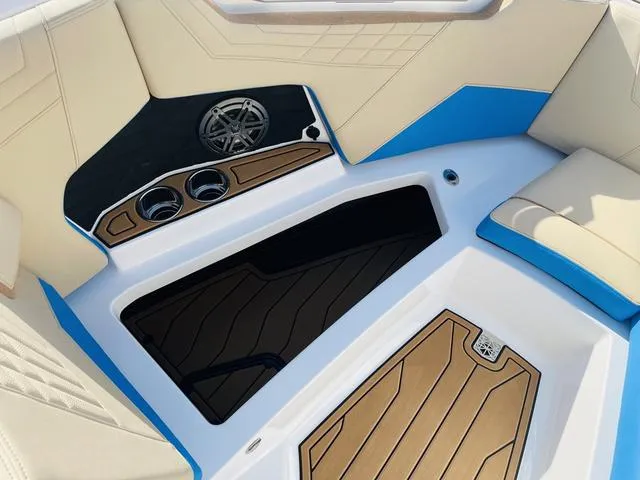 Slide: The Image of 2024 Nautique S23 boat interior with beige and blue seating, cup holders, and speaker. - 14