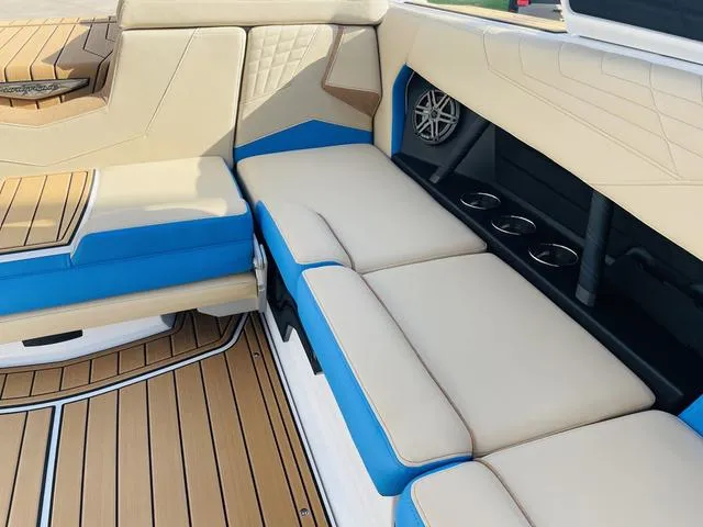 Slide: The Image of 2024 Nautique S23 boat interior with beige and blue seating, cup holders, and teak flooring. - 34