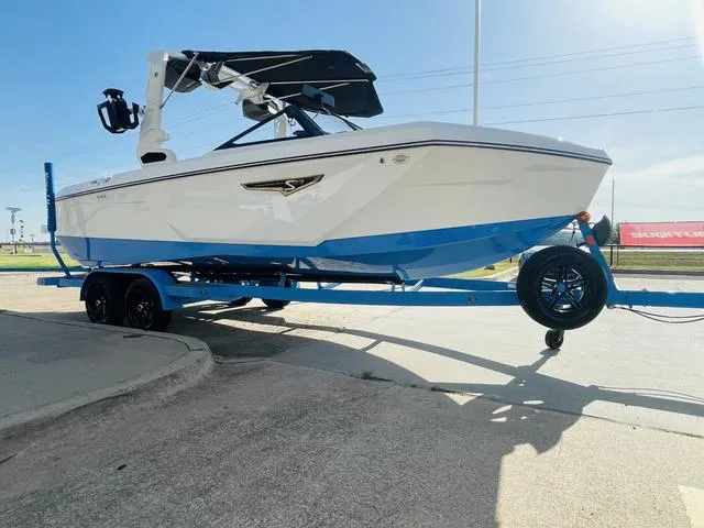 Slide: The Image of 2024 Nautique S23 boat on trailer, white and blue design, parked outdoors. - 4