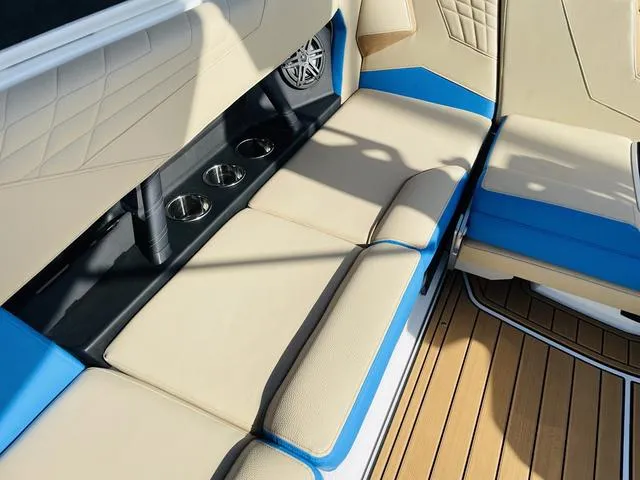 Slide: The Image of 2024 Nautique S23 boat interior with beige and blue seating, cup holders, and teak flooring. - 40