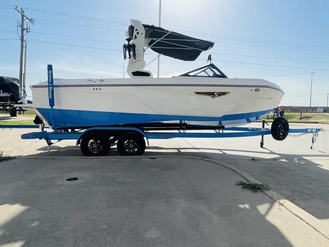 Slide: The Image of 2024 Nautique S23 boat on trailer, white and blue design, sunny day. - 5