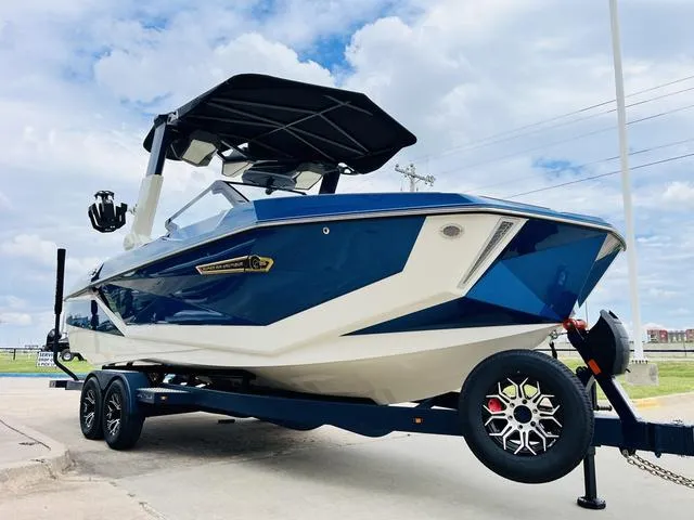 Slide: The Image of 2025 Nautique SUPER AIR G G25 boat on trailer, blue and white design, parked outdoors. - 4